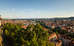 Panorama der Stadt Graz mit Uhrturm und roten Dächern im Sonnenschein.