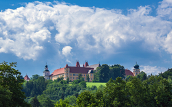 Schloss auf bewaldetem Hügel unter blauem Himmel mit Wolken.