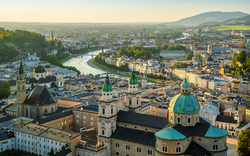 Stadtansicht von Salzburg mit Fluss und historischen Gebäuden im Abendlicht.
