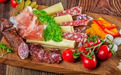 Verschiedene Wurst- und Käsesorten mit Tomaten auf einem Holzbrett serviert.
