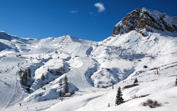 Schneebedeckte Berglandschaft mit Skiliften und Skifahrern, umgeben von blauem Himmel.
