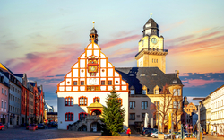 Historisches Gebäude in der Altstadt von Plauen bei Sonnenuntergang, mit Fachwerkfassade und einem hohen Uhrturm im Hintergrund.