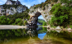 Felsformation mit natürlichem Steinbogen über einem Fluss, umgeben von grüner Vegetation.