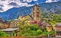 Steinkirche vor bewaldeten Bergen mit blühenden Sträuchern.