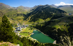 Blick auf ein Tal mit See, umgeben von grünen Bergen und wenigen Gebäuden.