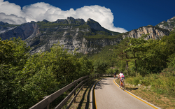 Zwei Radfahrer auf einem Weg in einer bergigen Landschaft mit Baumwuchs.