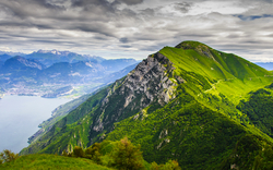 Grüne Berglandschaft mit See und Wolkenhimmel.