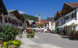 Straßenszene in bayerischem Dorf mit Bergen im Hintergrund bei sonnigem Wetter