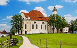 Weiße Kirche mit rotem Dach auf grünem Hügel, blauer Himmel im Hintergrund.
