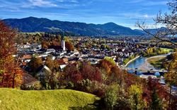 Blick auf eine malerische Stadt mit Fluss, Bergen und herbstlichem Laub.