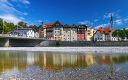 Fluss mit Uferhäusern und Kirche, blauer Himmel, sonnig.