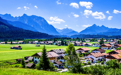 Dorf in alpiner Landschaft mit Bergen und blauem Himmel im Hintergrund.