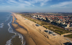 Luftaufnahme eines breiten Sandstrandes mit dahinter liegender Küstenstadt.