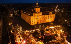 Luftaufnahme eines weihnachtlichen Marktes am Schlossplatz bei Nacht.