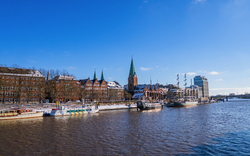 Flussansicht mit historischen Gebäuden und Schiffen bei blauem Himmel.