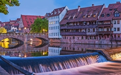 Fluss mit historischer Architektur und Brücke bei Abenddämmerung.