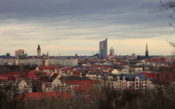 Stadtpanorama mit historischem und modernem Hochhaus im Hintergrund, wolkiger Himmel.