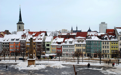 Verschneite bunte Altstadt mit Kirchturm im Hintergrund, klare Winterlandschaft.