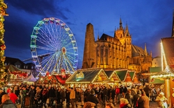 Weihnachtsmarkt mit geschmückten Ständen und beleuchtetem Riesenrad in der Abenddämmerung.