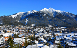 Verschneite Stadt vor schneebedeckten Bergen unter blauem Himmel.