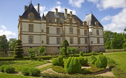 Schloss mit Garten und Buchsbaumhecken bei sonnigem Wetter.