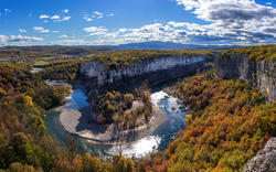 Fluss in einer Schlucht, umgeben von bewaldeten Hügeln und herbstlichem Laub.