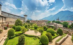 Gepflegter Garten mit Hecken, Architektur im Hintergrund, Berge am Horizont