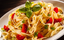 Tagliatelle mit Kirschtomaten, Basilikum und Kräutern auf weißem Teller.